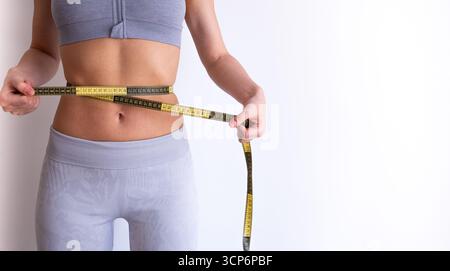 Frontbild einer Frau, die mit Klebeband den Taillenumfang misst. Lifestyle- und Gewichtsmanagement-Konzept für Fitness- und Diätartikel. Stockfoto