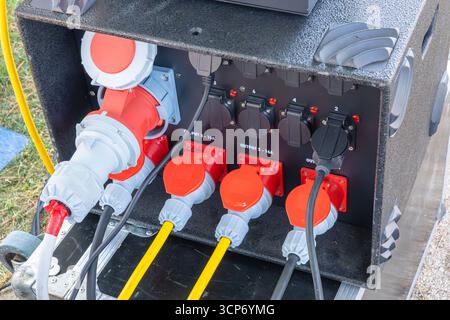Nahaufnahme eines tragbaren Schaltschrankes mit mehreren Steckdosen, roten Sicherheitsabdeckungen und gelben Kabeln, die für den Einsatz im Freien oder im Außeneinsatz bereit sind. Stockfoto