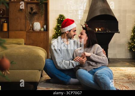 Frohe Weihnachten. Glückliches, junges, erwachsenes Paar, das sich in der Nähe von Weihnachtsbaum und Kamin umarmt. Glückliche Familie Mann Frau zu Hause. Menschen feiern gemeinsam Weihnachten und genießen die Winterferien zu Hause Stockfoto