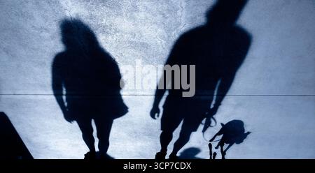 Schatten-Silhouette eines Paares und eines Mannes, der nachts mit einem Hund an der Leine geht Stockfoto