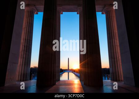 Lincoln Memorial Columns with Washington Monument Washington DC // WASHINGTON DC – die Kolonnade des Lincoln Memorial bietet einen Blick auf das Washington Monument und den Reflecting Pool während des Sonnenaufgangs. Das 1922 fertiggestellte Lincoln Memorial ehrt den 16. US-Präsidenten Abraham Lincoln und ist ein prominentes Wahrzeichen der National Mall. Das Washington Monument, ein Obelisk an George Washington, ist das höchste Bauwerk in Washington D.C. und ein zentrales Merkmal des monumentalen Kerns der Stadt. Das Design der Gedenkstätte, inspiriert von griechischen dorischen Tempeln, verfügt über 36 Säulen, die die 36 Stockfoto