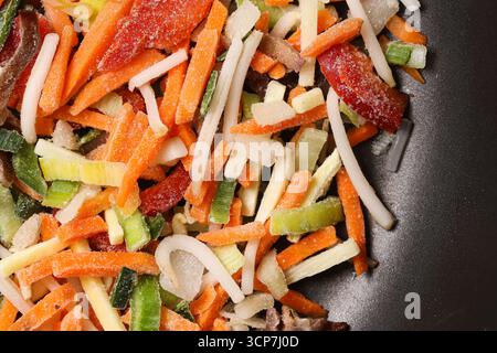 Gefrorenes Gemüse in der Pfanne mischen. Gehackte bunte Zutaten mit Karotten und Pfeffer. Gesundes Rohsortiment zum Kochen. Frisch geschnittene Zucchini-Zwiebeln. Stockfoto