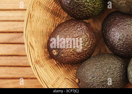 Frische, reife Avocados im Korb. Organische tropische Früchte aus der Nähe. Gesunde natürliche Lebensmittel reich an Vitaminen. Rustikaler Holzhintergrund mit exotischem Flair Stockfoto
