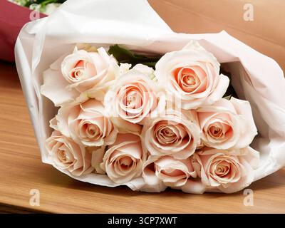 Strauß aus blassrosa Lachsrosen, in weißes Papier gewickelt, auf einem Holztisch platziert, Symbol für Liebe, Romantik und Hochzeitsfeiern. Stockfoto