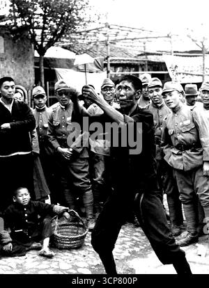 Nanking at Peace (5) - Ein chinesischer Straßenunterhalter, der einen Jongleur mit Essstäbchen und Schüssel macht. Japanische Garnisonstruppen auf einem Spaziergang schauen zusehends an. Februar 1939. (Foto von Japan Photo Library). Stockfoto