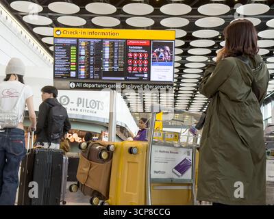 London Heathrow, Großbritannien – 24. September 2025: Fluggäste stehen in Warteschlange mit Gepäckwagen, während sie die Abflugbildschirme am Flughafen London Heathrow überprüfen Flüge vom Flughafen London Heathrow sind nach einem jüngsten Angriff auf die Flughafensoftware wieder normal. Quelle: Glosszoom/Alamy Live News. Stockfoto