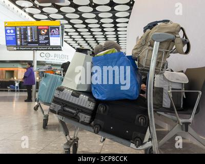 London Heathrow, Großbritannien – 24. September 2025: Fluggäste stehen mit Gepäckwagen an, während sie die Abflugbildschirme am Flughafen London Heathrow überprüfen. Flüge vom Flughafen London Heathrow sind nun wieder normal, nachdem vor Kurzem Ransom-Software-Angriffe auf Flughafensoftware stattgefunden haben. Quelle: Glosszoom/Alamy Live News. Stockfoto