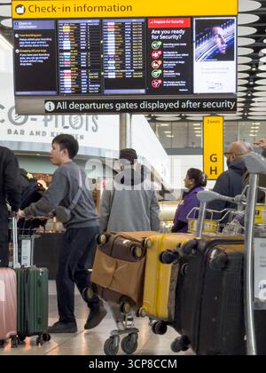 London Heathrow, Großbritannien – 24. September 2025: Fluggäste stehen in Warteschlange mit Gepäckwagen, während sie die Abflugbildschirme am Flughafen London Heathrow überprüfen Flüge vom Flughafen London Heathrow sind nach einem jüngsten Angriff auf die Flughafensoftware wieder normal. Quelle: Glosszoom/Alamy Live News. Stockfoto