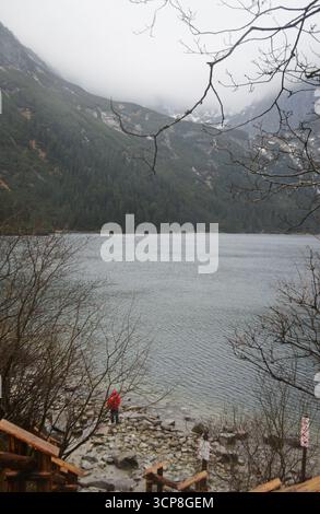 Wunderschöne Bergsee-Szene mit einer Person in Rot inmitten einer ruhigen Landschaft und unberührter natürlicher Schönheit, betont ruhiges Wasser und malerische Landschaft Stockfoto