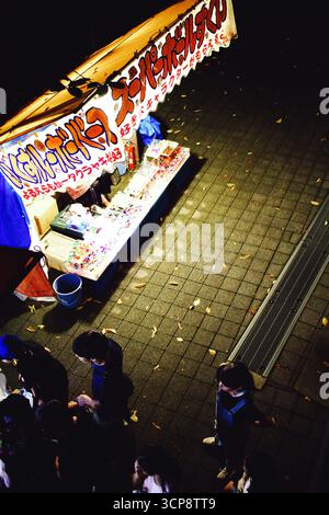 TOKIO, JAPAN – 20. September 2025: Hochwinkelblick einer Menge, die sich bei einem Sommerfest um einen glühenden Spielestand versammelt hat. Stockfoto