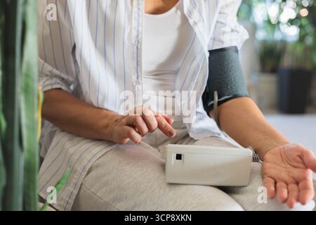 Ältere Frau mit digitalem Blutdruckmessgerät zu Hause, im Gesundheitswesen und im Wellness-Alltag Stockfoto