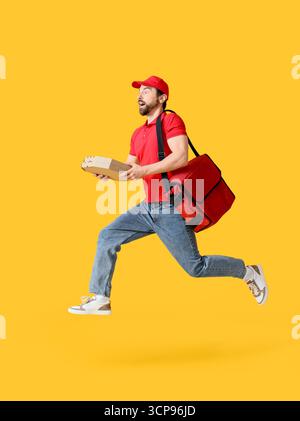 Schockierter männlicher Kurier mit Pizzakartons, die auf gelbem Hintergrund springen Stockfoto