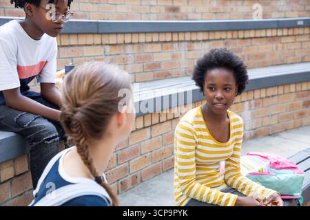 Diverse Teenager-Freunde unterhalten sich auf Schulbänken mit Rucksack, Wasserflasche, Kopierraum Stockfoto