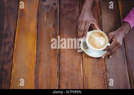 Afroamerikanischer Mann, der ein magentafarbenes Hemd trägt und Kaffeetasse und Kekse auf dem Kaffeetisch hält, Kopierraum Stockfoto
