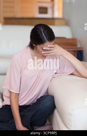 Frau, die neben dem hellen Sofa sitzt, Arm auf Armlehne im Wohnzimmer mit Mikrowelle Stockfoto