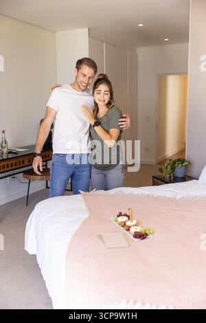 Paare stehen neben dem Bett im Schlafzimmer, halten sich in der Hand und untersuchen das Frühstückstablett Stockfoto
