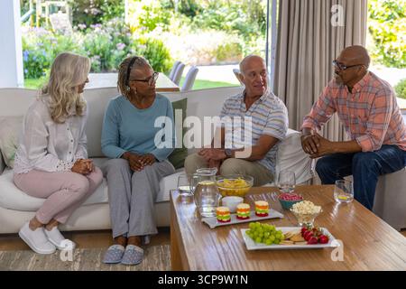 Verschiedene Seniorenfreunde unterhalten sich auf dem weißen Sofa im Wohnzimmer um den Couchtisch Stockfoto