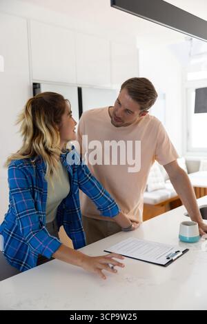 Ein Paar, das sich in der modernen Küche über die Insel lehnt und sich neben dem Keramikbecher die Papiere aus der Zwischenablage ansieht Stockfoto