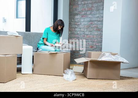 Pappkartons mit Luftpolsterfolie befinden sich auf gewebtem Teppich neben Sofa und roter Ziegelwand Stockfoto