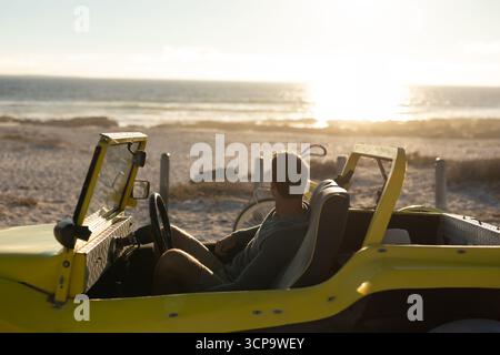 Mann sitzt in einem gelben Dünenwagen am Sandstrand und blickt mit dem Fahrrad in Richtung Ozean Horizont Stockfoto