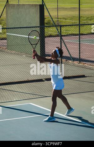Afroamerikanischer Teenager-Tennisspieler, der Schläger ausdehnt, Tennisball auf dem Platz schlägt, Kopierraum Stockfoto