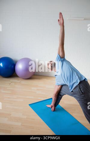 Männliches dehnendes Seitendreieck posiert auf blauer Yogamatte in der Nähe von Trainingsbällen im Studio, Kopierraum Stockfoto
