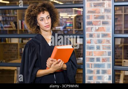 Oranges Hardcover-Buch auf Holztisch unter warmen Lichtern in Bibliothek mit Glasfächern Stockfoto