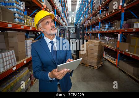 Lagerleiter mit gelbem Schutzhelm und Inspektion des Lagerbestands auf dem Tablet in der Nähe des Gabelstaplers Stockfoto