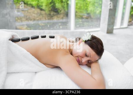 Weibliche Spa-Kundin, die eine Behandlung mit heißem Stein erhält, wobei schwarze Steine auf dem Tisch im Behandlungsraum liegen Stockfoto