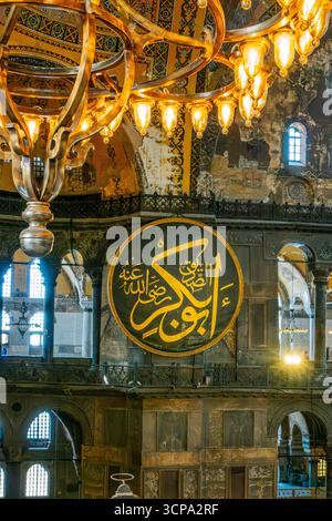 Osmanischer Kronleuchter Und Arabische Kalligrafiemedaillons In Der Hagia Sophia Istanbul. Byzantinische Architektur, Islamische Kunst, Goldene Beleuchtung, Historische Stockfoto