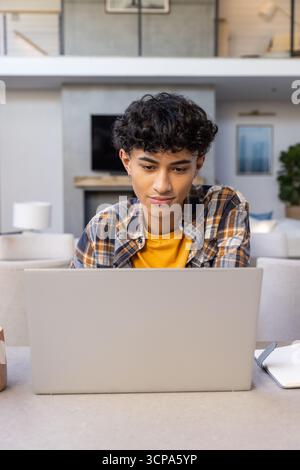 Asiatischer Mann tippt auf silbernem Laptop am Wohnzimmertisch mit Keramikbecher, Notizbuch Stockfoto
