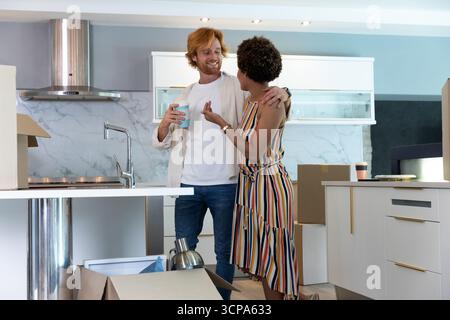 Diverse Paare stehen in der Küche und halten Kaffeetassen neben ungepackten Boxen mit Wasserkocher Stockfoto