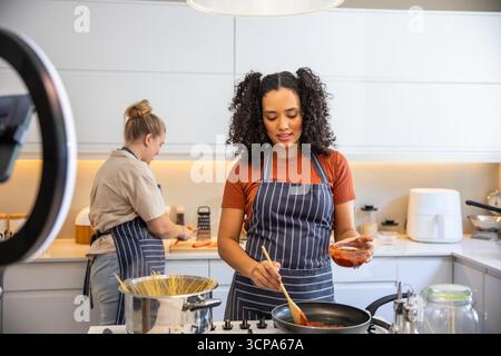 Diverse weibliche Freunde kochen zu Hause Küche Theke Rührsoße mit Topf, Ringlicht Stockfoto