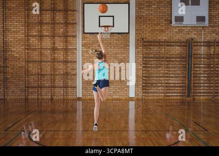 Weibliche Basketballspielerin springt in Richtung eines an der Wand befestigten Basketballkörpers im Fitnessstudio Stockfoto