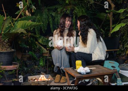 Winter, glückliche Frau Freundin genießt Outdoor Camp im Wald, Leute versammeln sich um eine gemütliche Feuerstelle Stockfoto