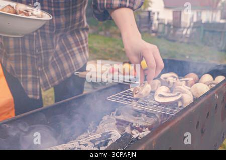 Zubereitung von gebratenen Pilzen auf dem Grill während eines Herbstpicknicks mit Rauch im Hintergrund Stockfoto