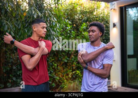 Verschiedene männliche Freunde, die auf der Terrasse die Arme über die Brust Strecken, tragen sportliche Hemden und Smartwatches Stockfoto