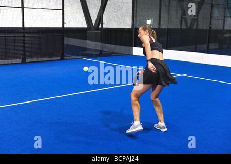 Weibliche Athletin in Sportkleidung, schwingender Schläger, schlägt neongrünen Ball auf dem Paddelplatz, Kopierraum Stockfoto