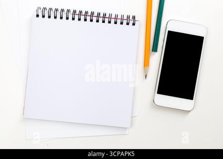 Leeres Notebook, Schreibwaren und Smartphone am Morgen auf einem weißen Schreibtisch Stockfoto