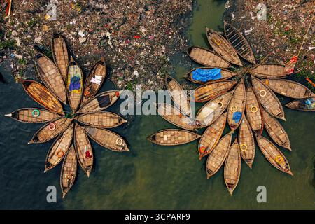 Aus der Vogelperspektive sehen Sie Boote, die in einem blumigen Muster auf der Wasseroberfläche zusammengebaut sind, vor dem Hintergrund von pulsierendem Müll und Trümmern, Flowers of Boats, Dhaka Division, Bangladesch. Stockfoto