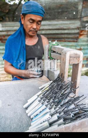 Männlicher Cebuano-Arbeiter, der Feuerwerkskörper für das neue Jahr in einem kleinen Freiluftbetrieb in Mactan Island, Cebu, zusammenbaut Stockfoto