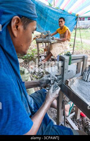 Männliche Cebuano-Arbeiter, die Feuerwerkskörper für das neue Jahr in einem kleinen Freiluftbetrieb in Mactan Island, Cebu, zusammenbauen Stockfoto