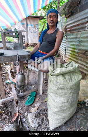 Männlicher Cebuano-Arbeiter, der Feuerwerkskörper für das neue Jahr in einem kleinen Freiluftbetrieb in Mactan Island, Cebu, zusammenbaut Stockfoto