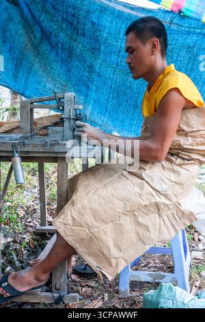 Männlicher Cebuano-Arbeiter, der Feuerwerkskörper für das neue Jahr in einem kleinen Freiluftbetrieb in Mactan Island, Cebu, zusammenbaut Stockfoto