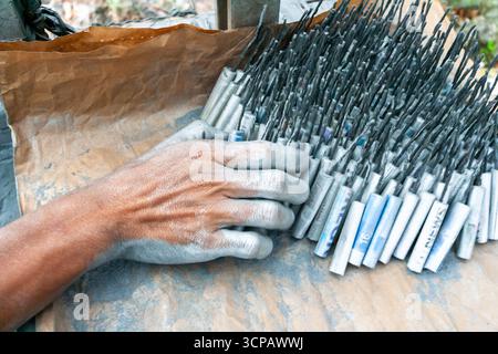 Männlicher Cebuano-Arbeiter, der Feuerwerkskörper für das neue Jahr in einem kleinen Freiluftbetrieb in Mactan Island, Cebu, zusammenbaut Stockfoto