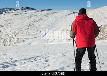 Männlicher Skier mit roter Winterjacke, der die Skistöcke rechts vom verschneiten Hang hält, Kopierraum Stockfoto