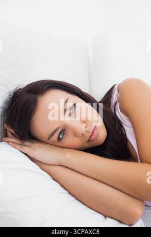 Weiße Erwachsene Frau, die auf dem Bett liegt und Kopf auf Kissen im Schlafzimmer mit weißer Steppbettwäsche liegt Stockfoto
