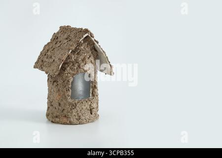 Ein kleines, handgefertigtes Modellhaus aus recyceltem Zellstoff mit einer natürlichen rauen Oberfläche und offenen Fenstern, auf einem glatten weißen Hintergrund. Stockfoto
