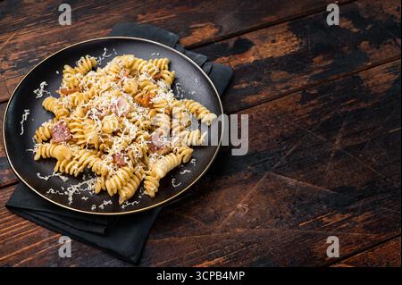 Italienische Carbonara-Pasta mit knusprigen Speckstückchen auf einem Teller. Hölzerner Hintergrund. Draufsicht. Stockfoto