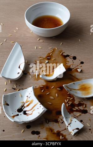Eine kreative und künstlerische Darstellung einer zerbrochenen Schüssel mit Sauce und Reis, die überall verstreut sind Stockfoto